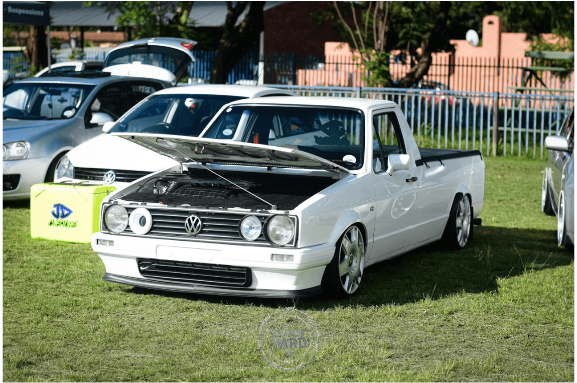White lowered Volkswagen pickup displayed at a car gathering with its bonnet open