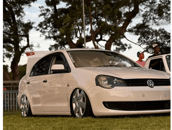 Cream lowered Volkswagen hatchback with polished wheels at an outdoor gathering